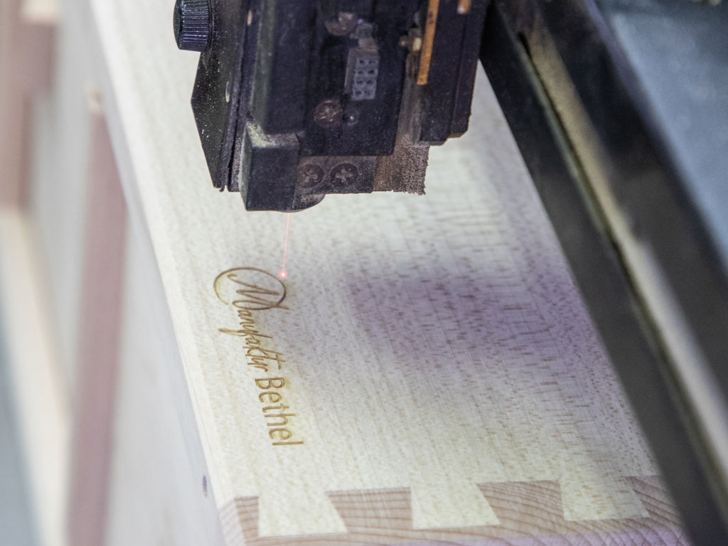 Eine Graviermaschine graviert ein Schriftzug in ein Holzstück