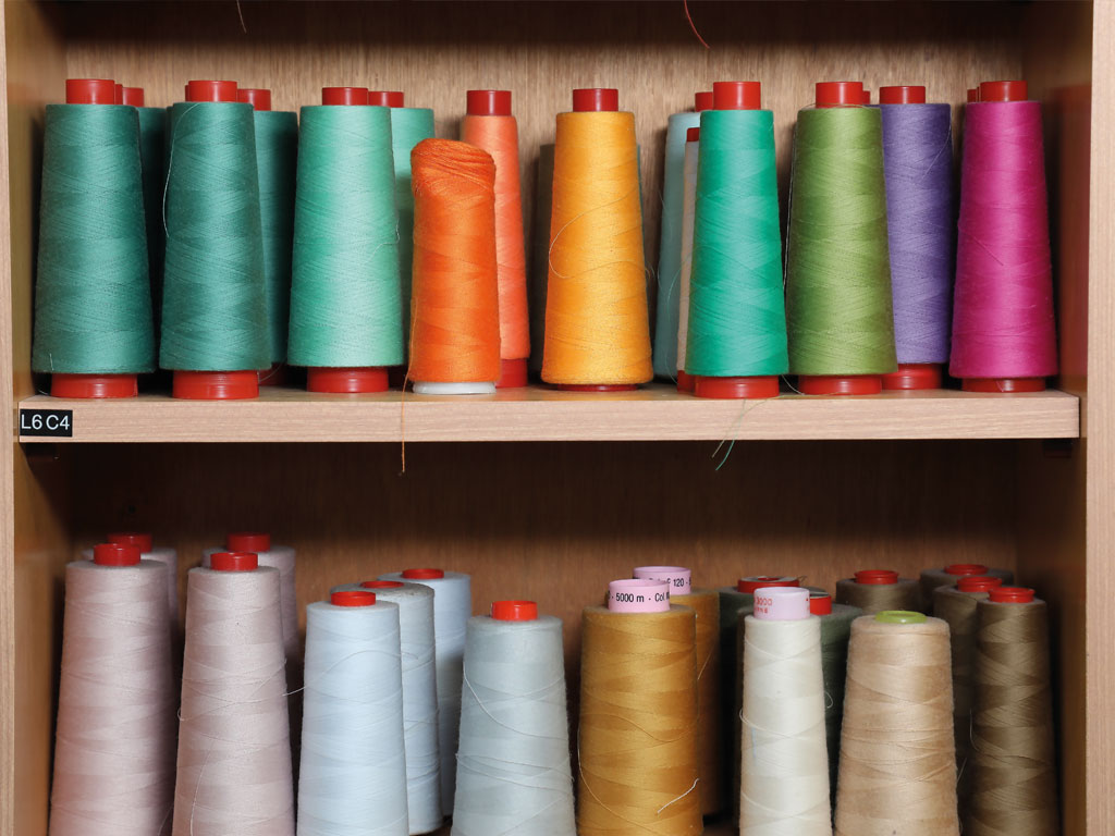 In einem braunen Schrank stehen bunte Rollen Nähgarn, verteilt auf zwei Regalfächer innerhalb des Regals.