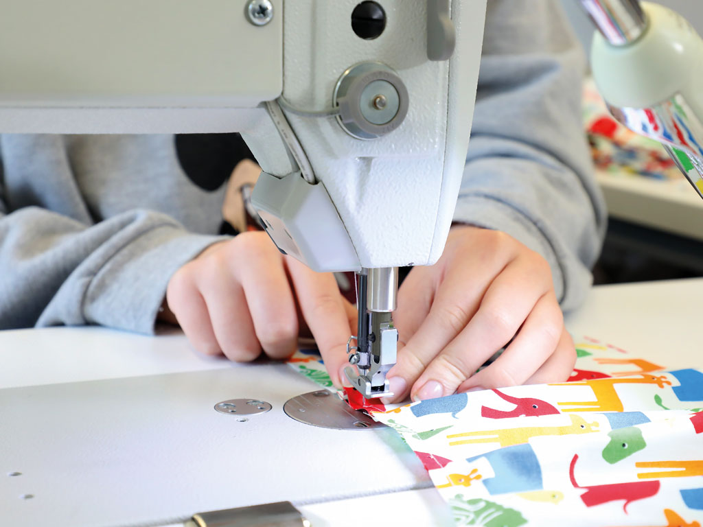 Ein fröhlich gemusterter Stoff mit bunten Tieren wird sorgfältig mit der Nähmaschine zusammengenäht.