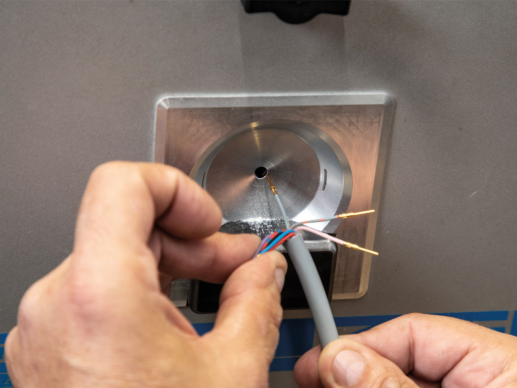 Eine Person hält ein aufgeschnittenes Kabel vor eine Maschine zur Weiterverarbeitung.