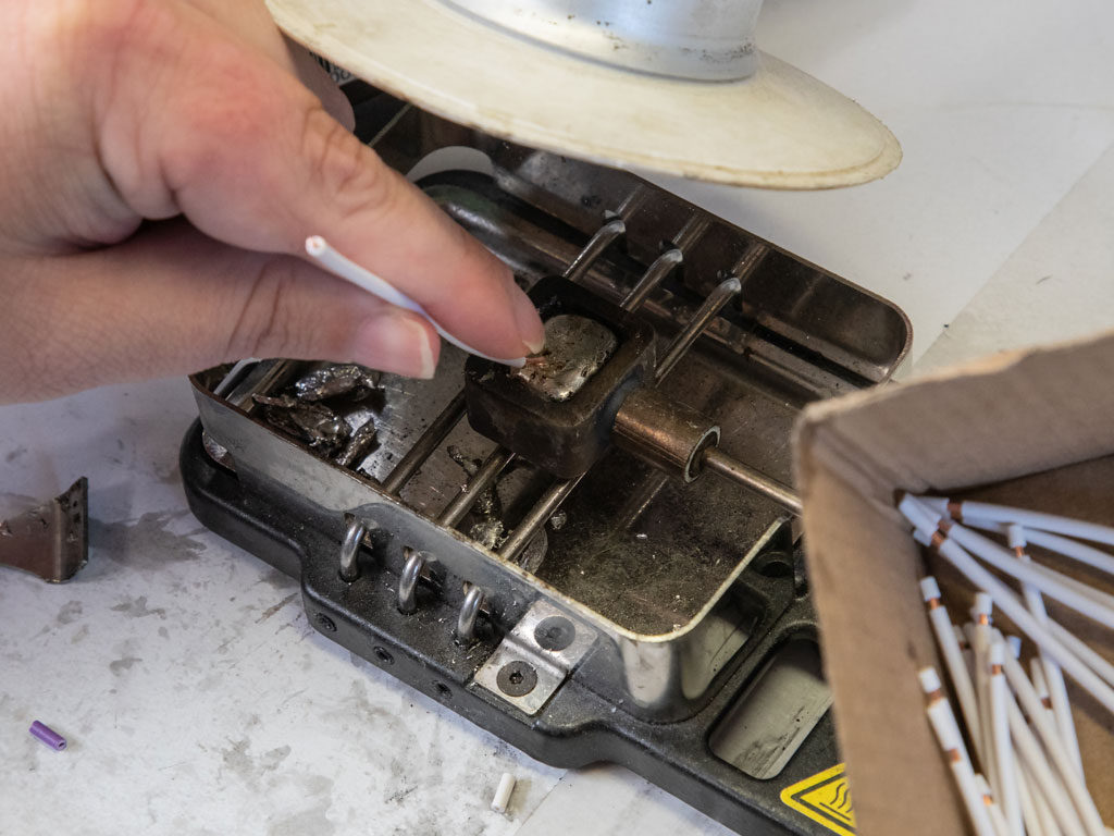 Ein kurzes Kabelstück befindet sich in einer geöffneten Maschine und wird dort weiterverarbeitet. Direkt daneben steht eine Schachtel mit weiteren, gleichartigen Kabelstücken.